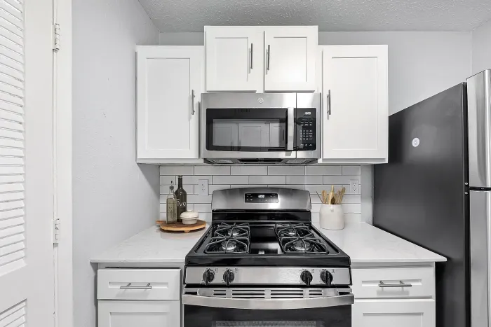 Modern apartment kitchen with stainless steel gas range, built-in microwave, white shaker cabinets, subway tile backsplash, and quartz countertops.