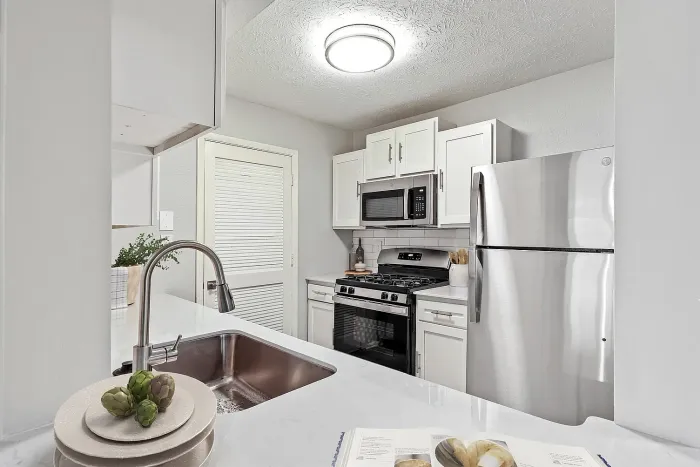Bright apartment kitchen with stainless steel appliances, farmhouse-style sink, quartz countertops, white shaker cabinets, and subway tile backsplash.