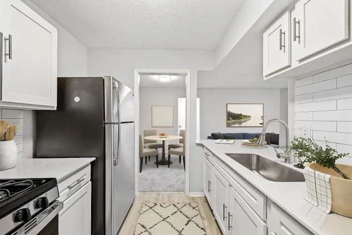 Open-concept apartment kitchen with stainless steel appliances, quartz countertops, white shaker cabinets, subway tile backsplash, and view into dining and living area.