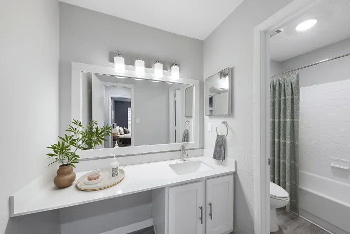 Modern apartment bathroom with large vanity mirror, quartz countertop, white shaker cabinets, updated lighting, and tub-shower combination.