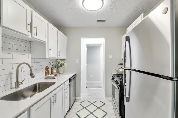 Galley-style apartment kitchen with stainless steel appliances, quartz countertops, white shaker cabinets, subway tile backsplash, and modern finishes.