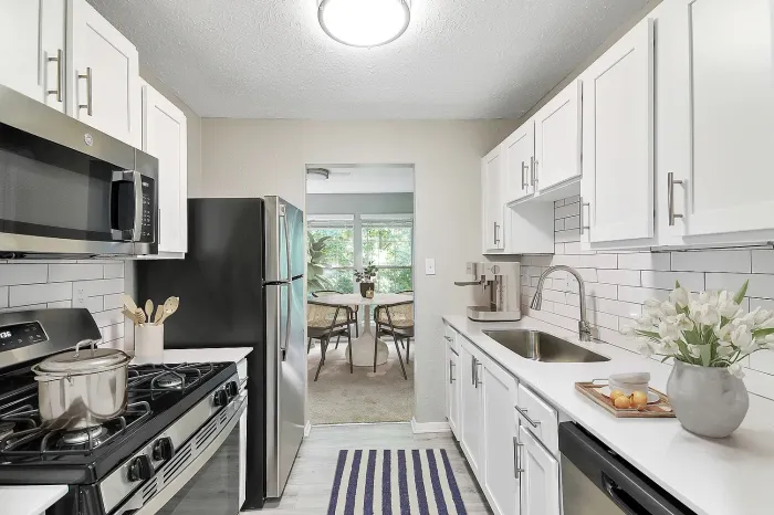 Updated apartment kitchen with stainless steel appliances, quartz countertops, white shaker cabinets, subway tile backsplash, and adjacent dining area with natural light.