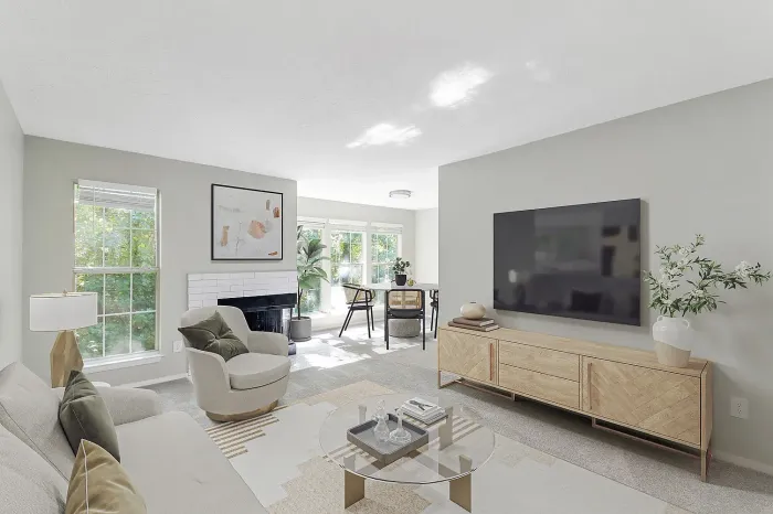 “Modern apartment living room with wall-mounted TV, decorative fireplace, plush carpeting, large windows, and open-concept layout with natural light.