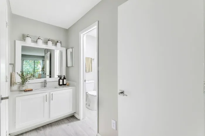 “Modern apartment bathroom with quartz vanity, large mirror, white cabinetry, updated lighting, and adjacent tub-shower area.