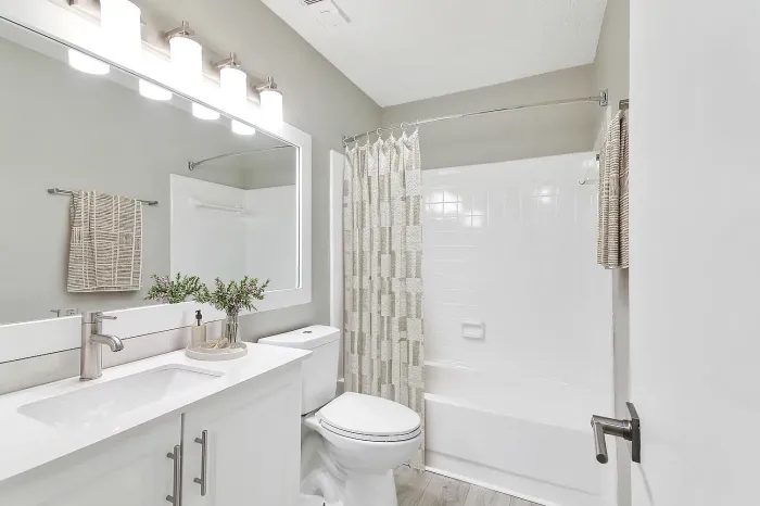 Bright apartment bathroom with white vanity, modern lighting, bathtub-shower combo, and neutral finishes.