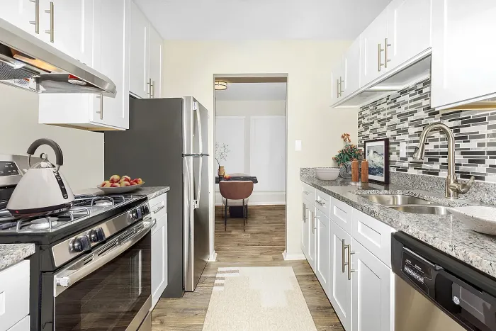 Updated apartment kitchen with white cabinets, granite countertops, subway tile backsplash, stainless steel appliances, and wood-style flooring.