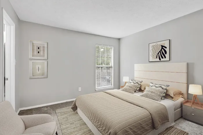 Bright apartment bedroom with neutral decor, large bed, soft carpeting, bedside lighting, and natural light from window.