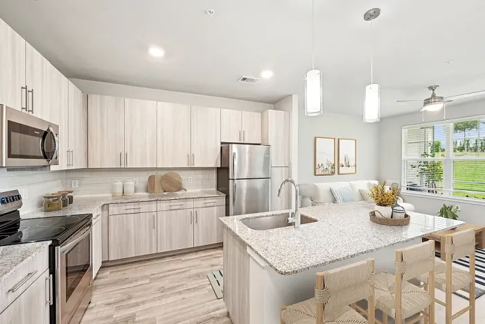 Modern open-concept kitchen with sleek stainless steel appliances, stylish light wood cabinetry, and a chic island adjacent to a cozy living area with large windows.