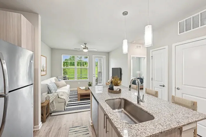 Bright and modern open-concept living area with sleek kitchen island, stylish pendant lighting, and inviting lounge space overlooking lush greenery.