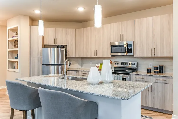 Bright, modern kitchen with stainless steel appliances, light wood cabinetry, and a granite island with bar seating.