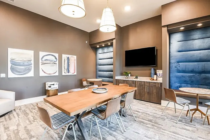 Modern clubhouse meeting and dining space with a large communal table, pendant lighting, built-in seating nooks, and a media area with a mounted TV.
