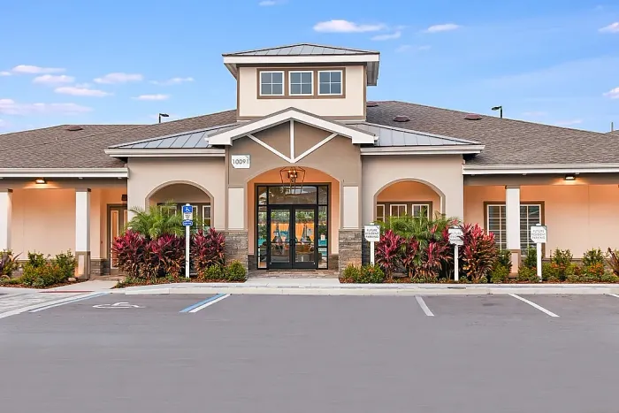 Exterior of a modern apartment community leasing office with a covered entrance, landscaped surroundings, and parking in front.