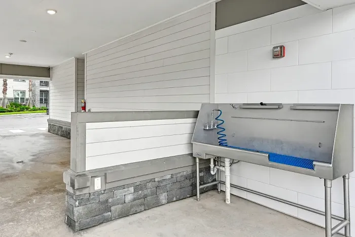 Covered pet wash station with a stainless steel tub, handheld sprayer, and drainage, located in a clean, sheltered outdoor area of the community.