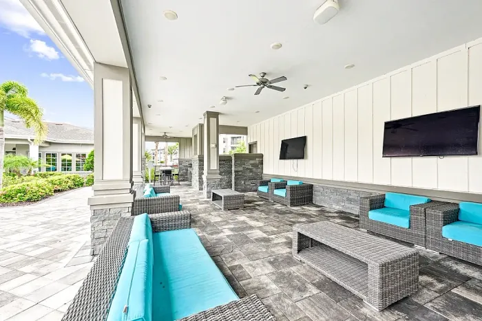 Covered outdoor lounge area with cushioned seating, ceiling fans, and mounted TVs, offering a comfortable space for relaxing and gathering within the community.