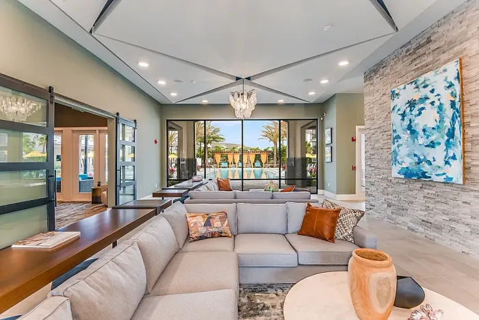Elegant clubhouse lounge with a large sectional sofa, modern decor, and a statement chandelier, featuring expansive windows that overlook the resort-style pool area.