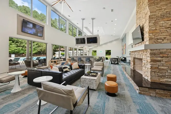 Spacious modern clubhouse with high ceilings, large windows, a stone fireplace, lounge seating, bar area, and views of the outdoor pool.