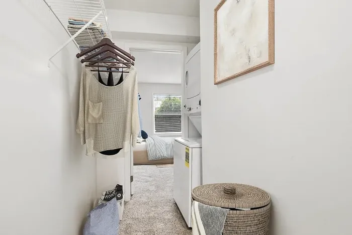 Inviting laundry area with modern stacked washer and dryer, cozy bedroom view in the background, and stylish decor.