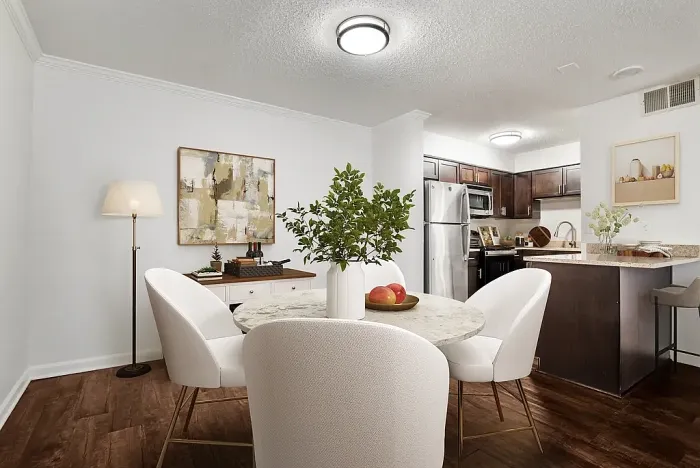 Modern dining area with elegant white chairs and a round marble table, adjacent to a sleek kitchen with dark wood cabinetry and stainless steel appliances.