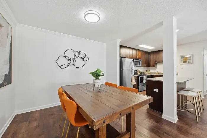 Chic dining area with a rustic wooden table and vibrant orange chairs, adjacent to a modern kitchen featuring stainless steel appliances and a sleek breakfast bar.