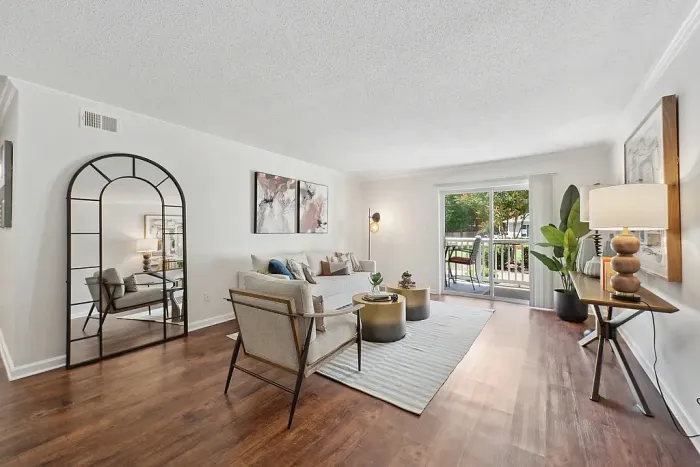 Elegant living room with hardwood floors, stylish decor, and natural light from a large sliding glass door leading to a balcony with garden views.