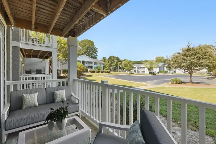 Charming apartment balcony with cozy seating overlooking a lush, green landscape and vibrant community setting.