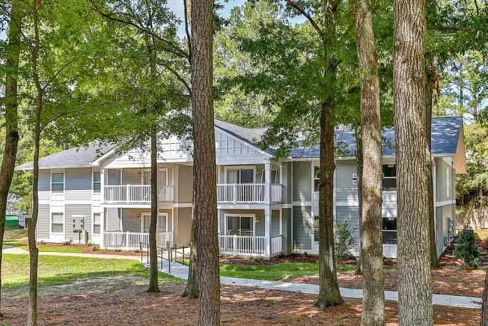 Inviting grey and white apartment complex with lush green landscaping, featuring charming balconies and surrounded by mature trees.