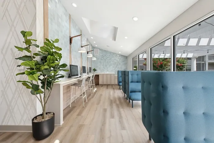 Bright resident lounge and workspace with booth seating, a row of computers, pendant lighting, large windows, and modern finishes.