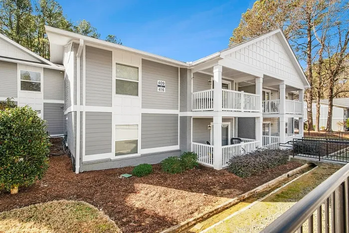 Charming two-story apartment building with pristine white balconies, surrounded by lush greenery and vibrant landscaping.