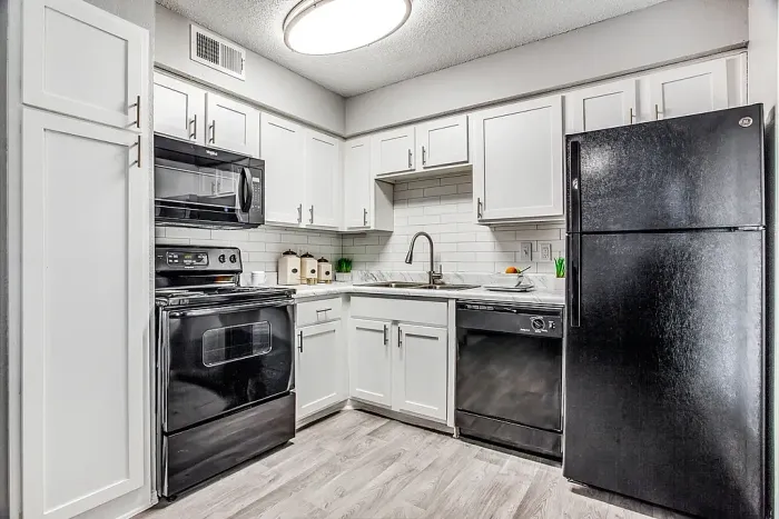 Modern kitchen with white cabinets, marble-style countertops, and black appliances, including an electric stove, microwave, dishwasher, and refrigerator. Features a subway tile backsplash, hardwood-style flooring, and simple countertop decor for a clean, updated look.