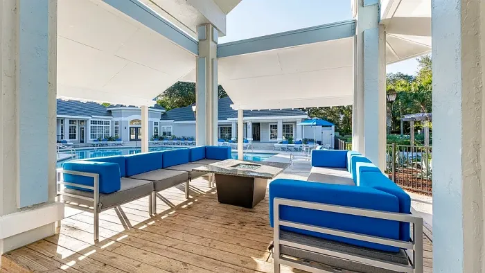 Outdoor covered seating area with blue cushioned sofas, fire pit table, and views of resort-style pool.