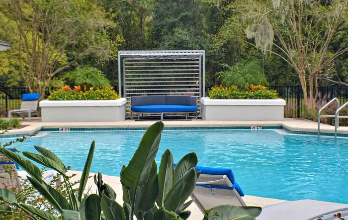 Resort-style pool with cushioned seating under a cabana and lush landscaping.