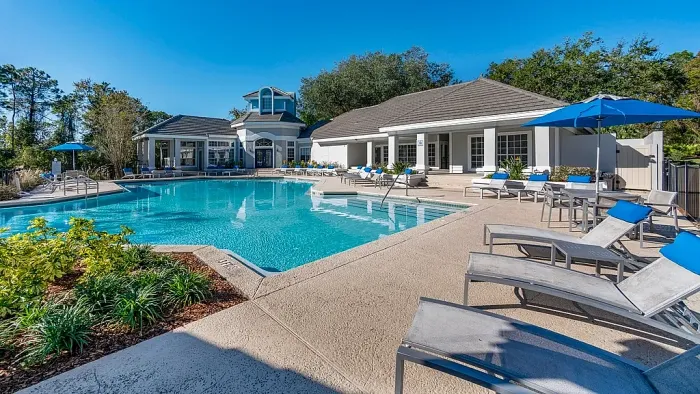 Resort-style pool with lounge seating, blue umbrellas, and clubhouse.