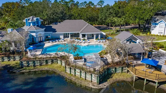 Aerial view of resort-style swimming pool, clubhouse, and waterfront deck with outdoor seating.