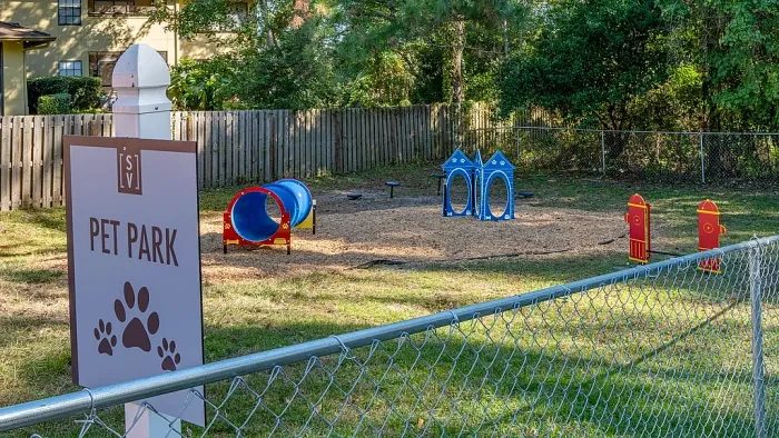 Fenced dog park with agility equipment, tunnels, and play structures.