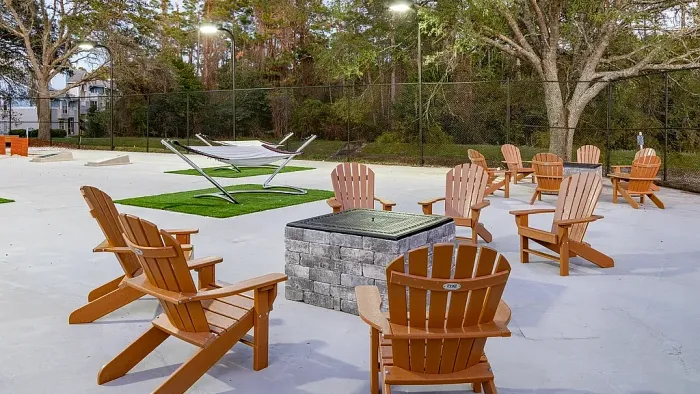 Outdoor fire pit lounge with Adirondack chairs, hammocks, and open seating area.