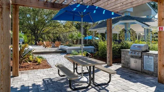 Outdoor kitchen area with built-in grill, pergola, picnic table, and landscaped seating.