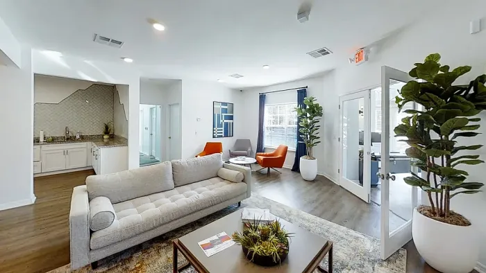 Clubhouse lounge with modern seating, kitchen area, hardwood-style flooring, and large windows.