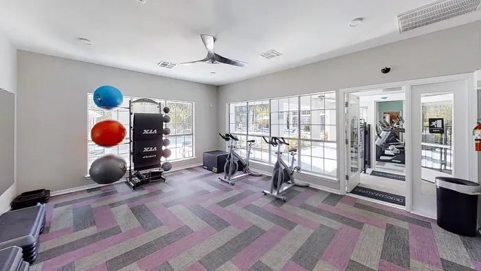 Fitness center with cardio equipment, stationary bikes, free weights, and large windows.