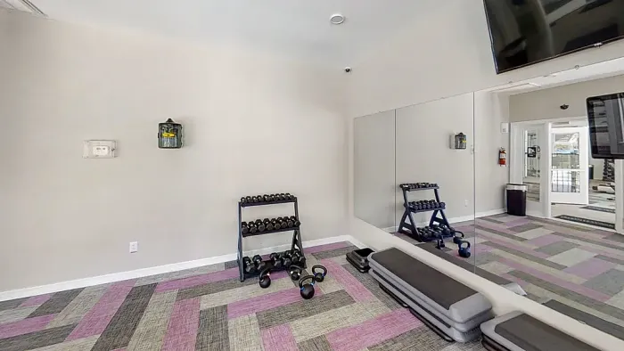 Fitness center with dumbbells, mirrored wall, step platform, and open workout space.