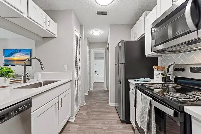 Galley-style kitchen with stainless steel appliances, white cabinetry, and modern finishes.
