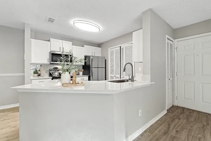 Open-concept kitchen with breakfast bar, white cabinetry, stainless steel appliances, and tile backsplash.