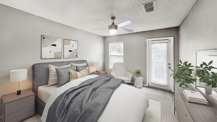 Bright bedroom with neutral finishes, featuring a large bed, ceiling fan, bedside tables, and a sitting area with access to a private patio.
