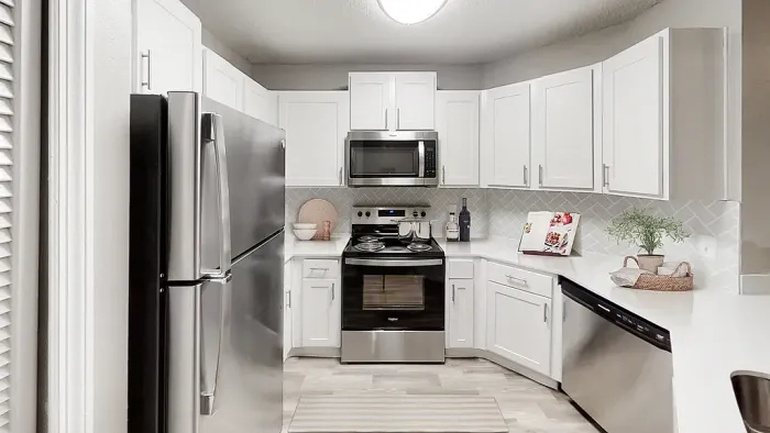 Bright kitchen with white cabinetry, stainless steel appliances, white quartz countertops, and a herrigbone tile backsplash in a clean, modern layout.
