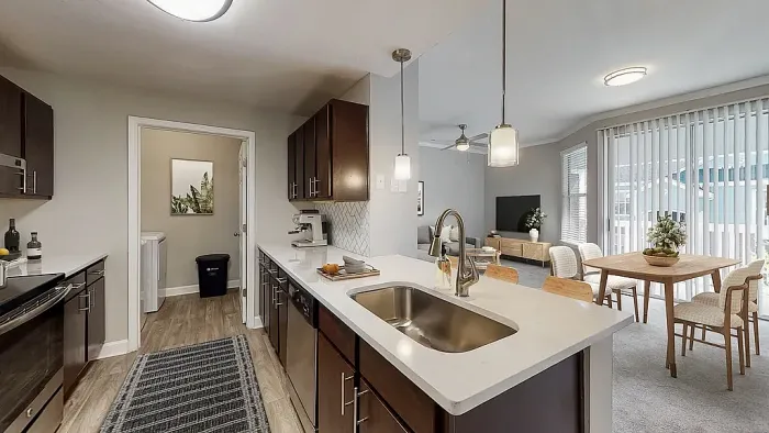 Modern open-concept apartment kitchen with dark wood cabinetry, stainless steel appliances, white quartz-style countertops, pendant lighting, and a spacious breakfast bar overlooking the dining and living areas.