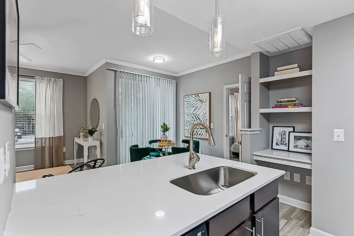 Modern open-concept apartment kitchen with white quartz-style countertops, dark wood cabinetry, pendant lighting, built-in shelving, and a breakfast bar overlooking the dining and living areas with contemporary decor.
