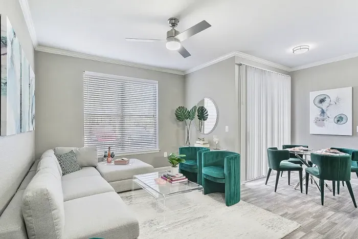 Modern open-concept apartment living and dining area with a sectional sofa, emerald green accent chairs, wood-style flooring, contemporary artwork, and a dining space with velvet seating and natural light.