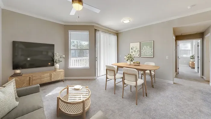 Bright open-concept apartment living and dining area with neutral tones, plush carpeting, large windows for natural light, contemporary furnishings, and access to a private balcony or patio.