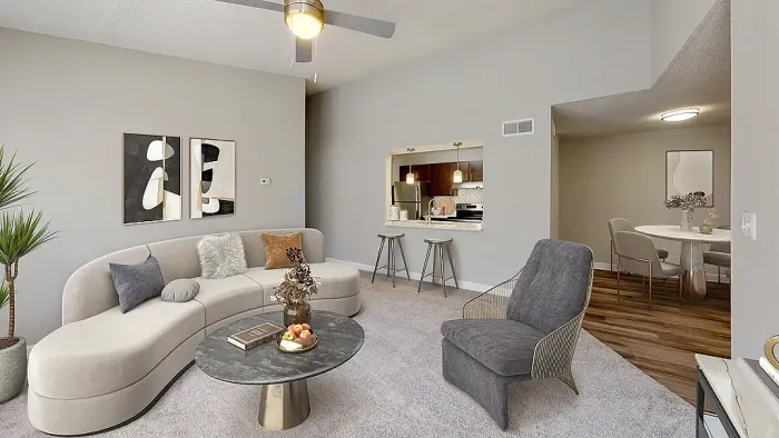 Modern apartment living and dining area with plush carpeting, contemporary furnishings, vaulted ceilings, neutral tones, and a pass-through kitchen with pendant lighting and bar seating.