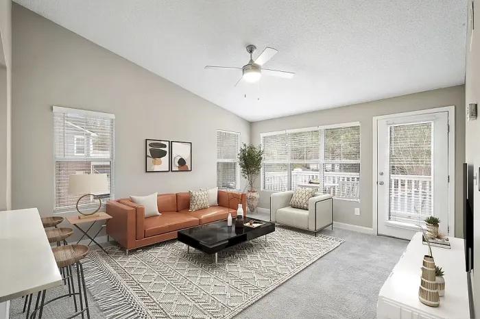 Bright apartment living room with vaulted ceilings, plush carpeting, contemporary furnishings, large windows for natural light, and access to a private balcony or patio.