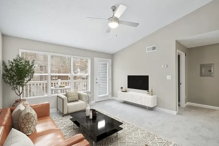 Bright apartment living room with vaulted ceilings, plush carpeting, large windows for natural light, contemporary furnishings, and access to a private balcony or patio.